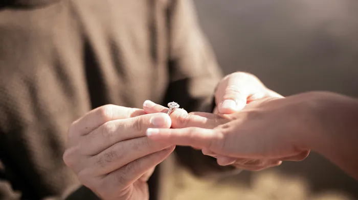 A hand slipping an engagement ring onto a partner's finger