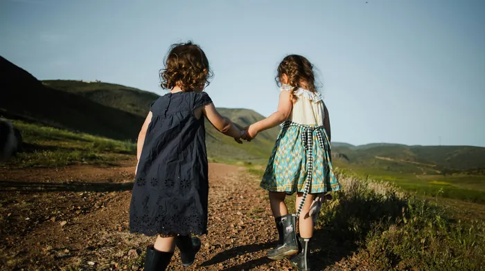 Two little girls holding hands as they walk along a hillside track