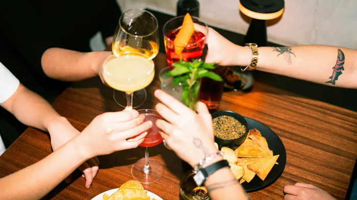 Friends raising their glasses in a toast across a table of drinks and snacks