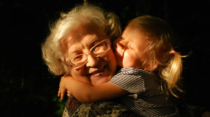 A grandmother with white hair and glasses sharing a warm hug with a young child