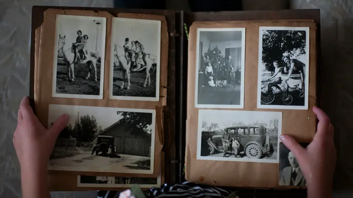 Hands holding open an old family album of black-and-white photographs